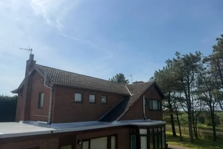 Detached brick house with a pale grey flat roof over the ground floor, under a blue sky