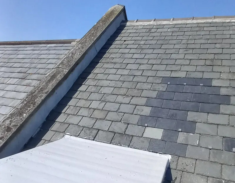 Slate roof with a patch of new replacement slates under a blue sky